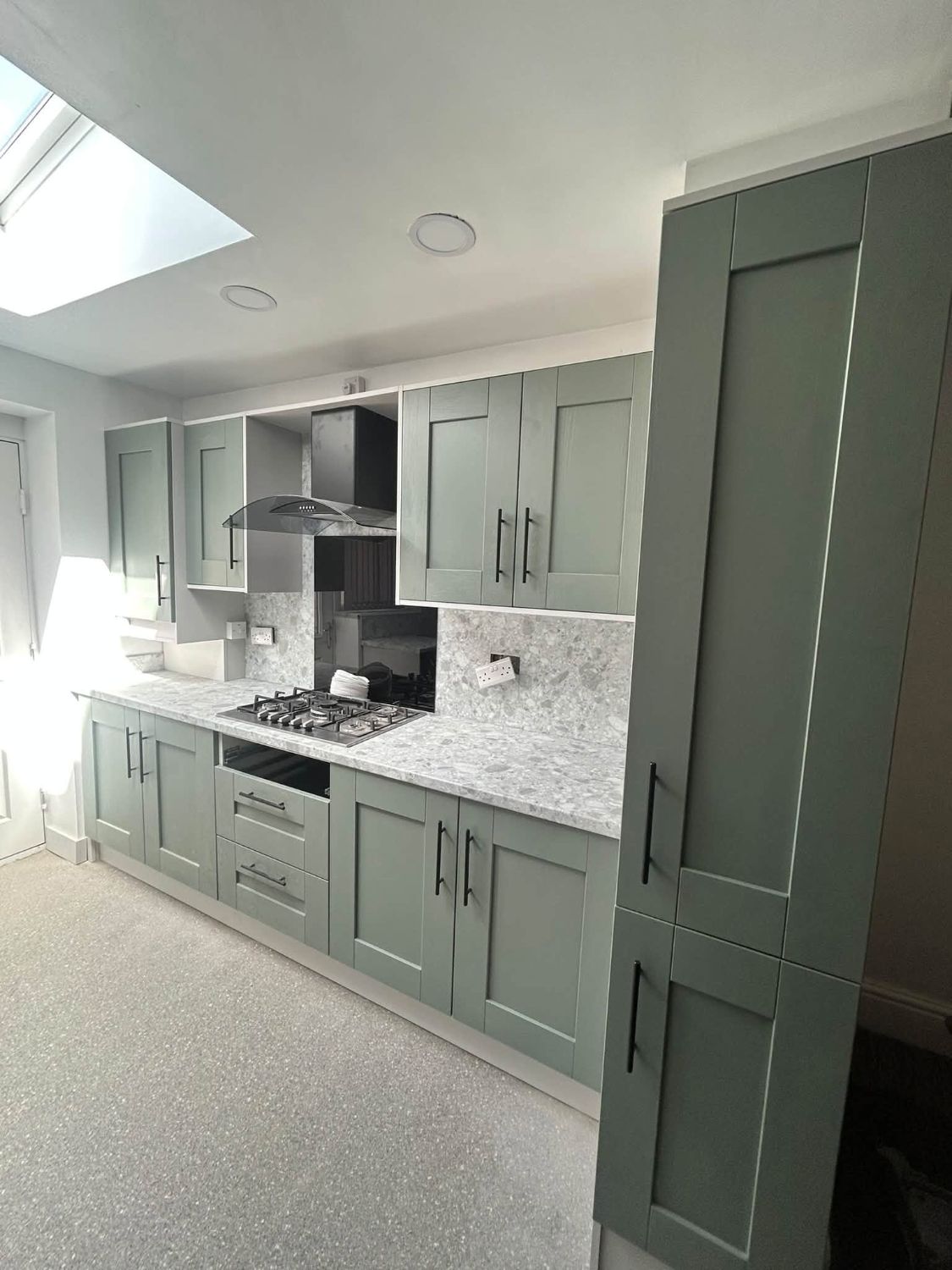 Sage green shaker kitchen with black bar handles and terrazzo worktop