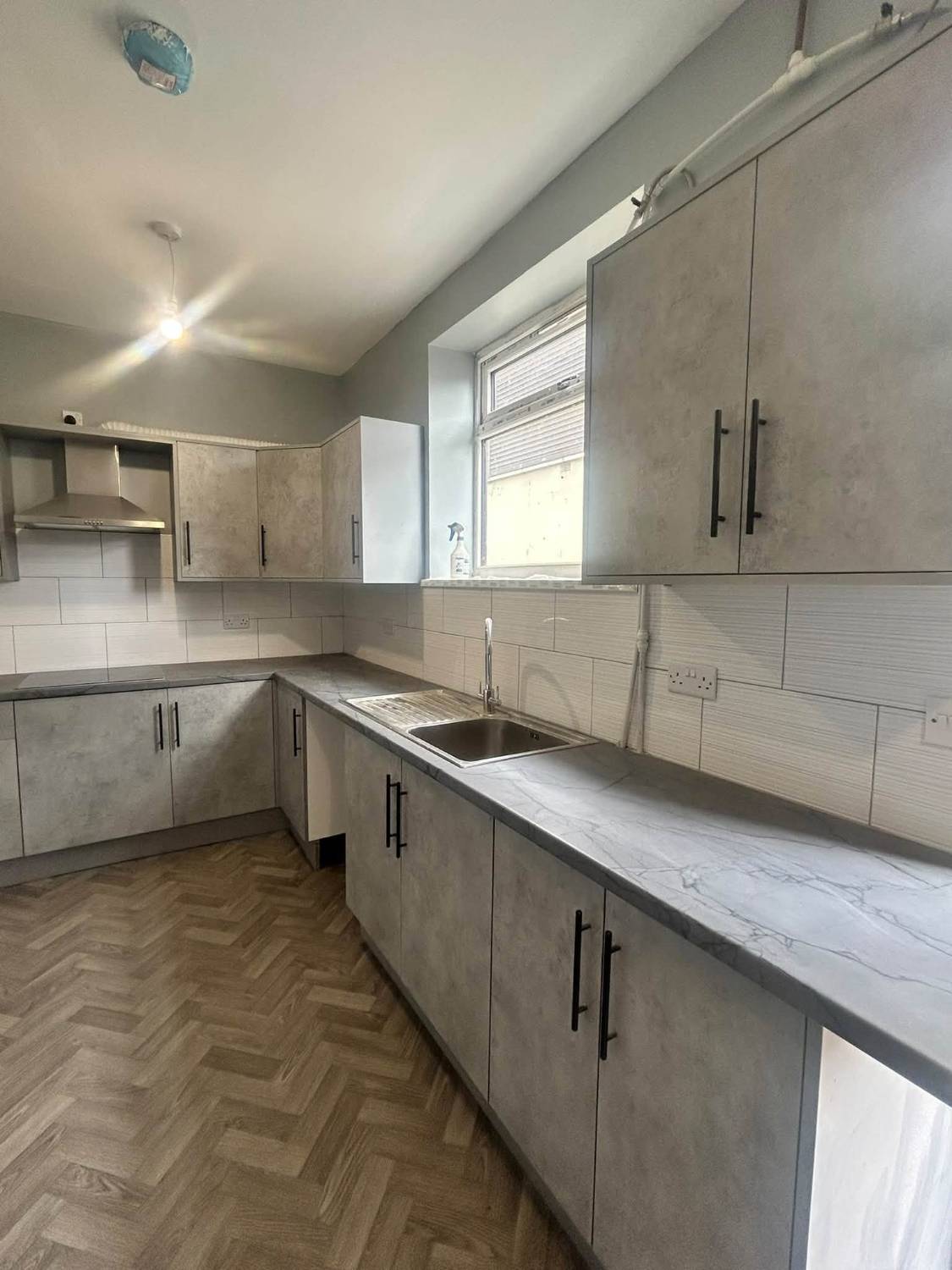 Light grey stone-effect kitchen with black handles and herringbone floor